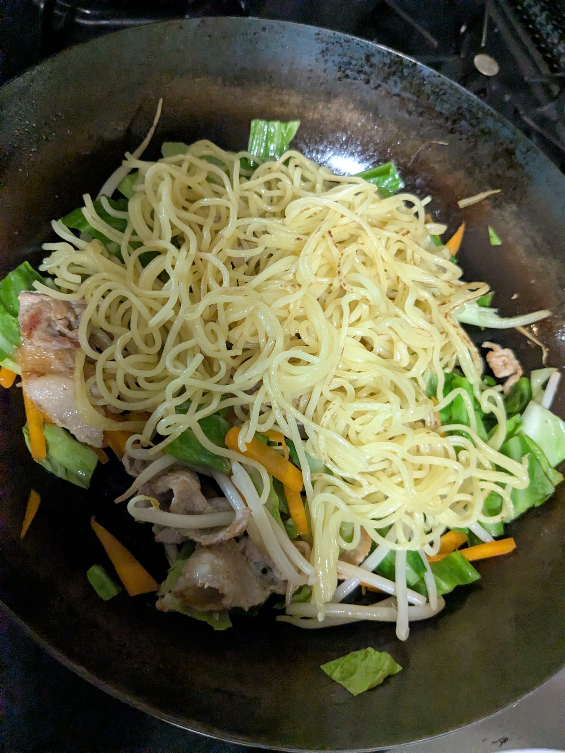 炒めた野菜の上に麺を戻した鉄フライパン