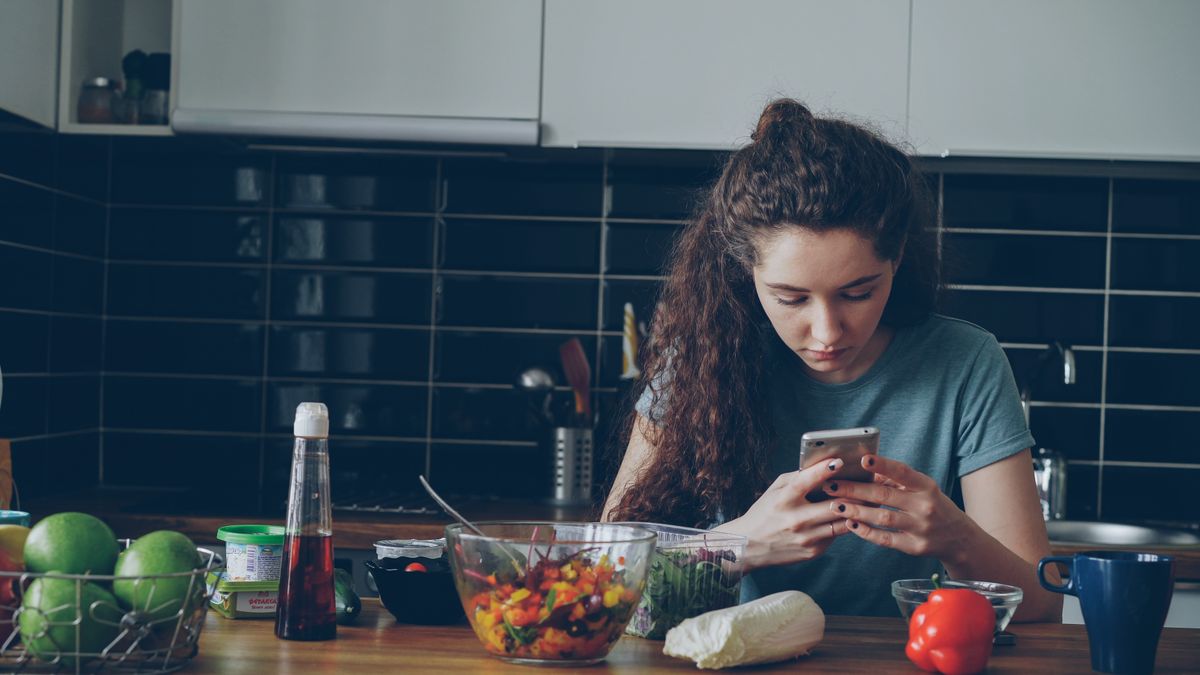 キッチンでスマートフォンを見ている女性